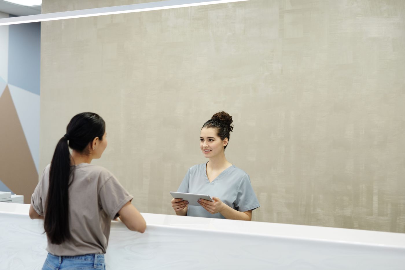 Recepcionista sorrindo enquanto atende uma paciente no balcão